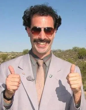 Borat, with a moustache and grey suit, giving two thumbs up