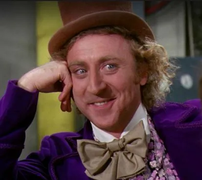 Gene Wilder as Willy Wonka in a purple coat and top hat, chin on hand, smirking