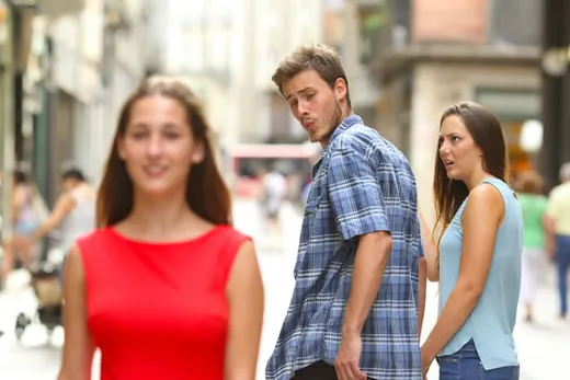 A man on a street turning to look at a woman in red while his girlfriend stares at him, outraged