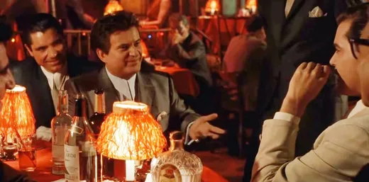 Joe Pesci as Tommy DeVito at a crowded restaurant table, staring menacingly