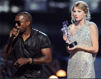 Kanye West holding a microphone on stage next to Taylor Swift, who holds an award