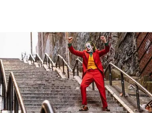 The Joker in a red suit dancing triumphantly down a long city staircase