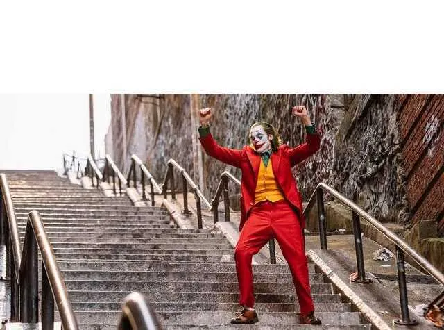 The Joker in a red suit dancing triumphantly down a long city staircase