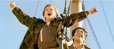Two young men at the bow of a ship, one with his arms spread wide, shouting
