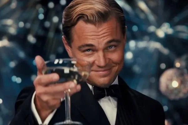 Jay Gatsby in a tuxedo, smiling and raising a glass of champagne