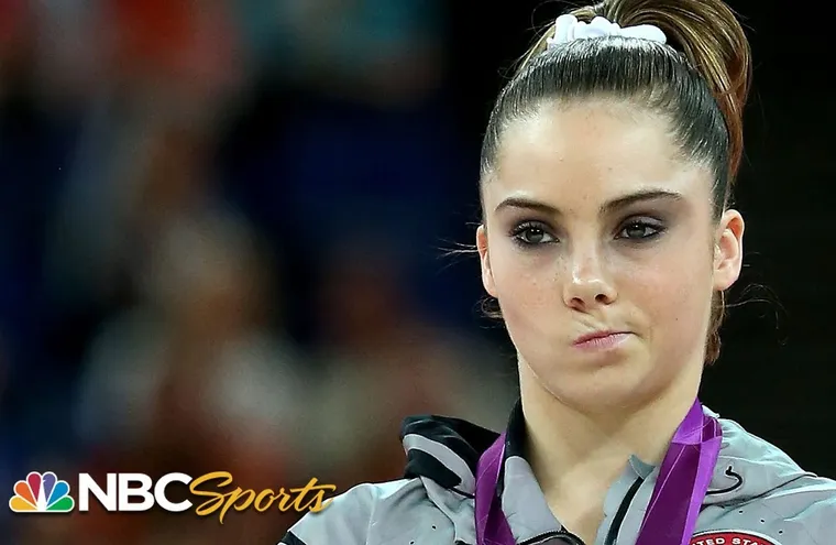 A gymnast in a leotard on a medal podium, lips pursed and eyebrow raised