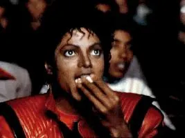 Michael Jackson in a red jacket in a dark cinema, eating popcorn and smiling