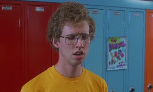 Napoleon Dynamite with curly hair and glasses in front of school lockers