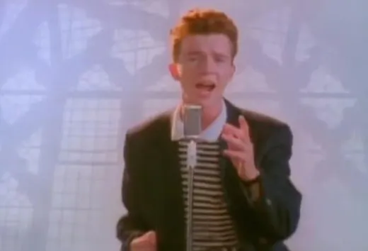Rick Astley in a trench coat, dancing in front of a brick wall