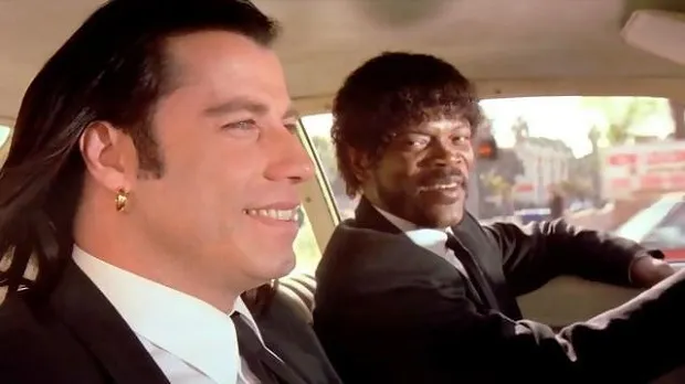 Jules and Vincent in black suits sitting in a car, talking