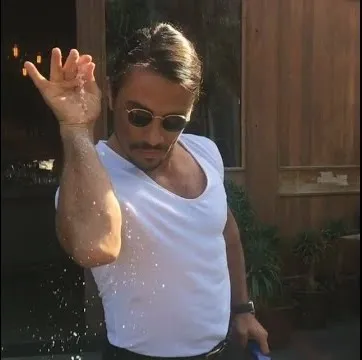 A man in sunglasses and a white T-shirt sprinkling salt from high above with a bent wrist