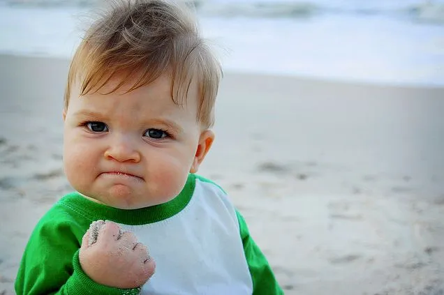 A toddler on a beach clenching a fist full of sand with a determined, satisfied face