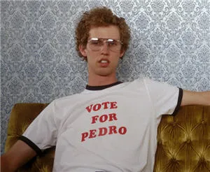Napoleon Dynamite with curly hair and glasses, in a white T-shirt reading "Vote for Pedro"