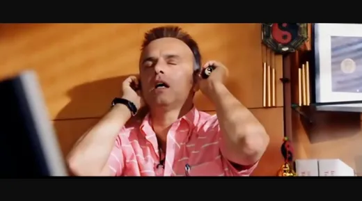 A man in a pink shirt with his hands on his temples, eyes closed, breathing deeply