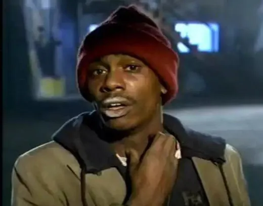 Dave Chappelle as Tyrone Biggums in a red beanie, scratching his neck and looking eager
