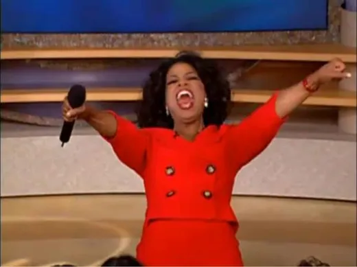 Oprah Winfrey in a red dress on stage, arms raised in excitement