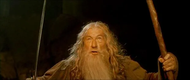 Gandalf in grey robes holding his staff and sword, shouting on a narrow bridge